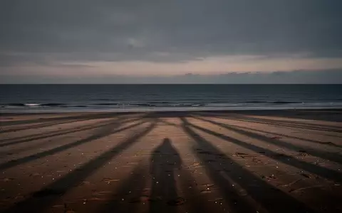 Ein einsamer, leerer Strand bei Dämmerung mit langen Schatten auf dem Sand und Blick auf das ruhige Meer. - Foto: über boerse-global.de