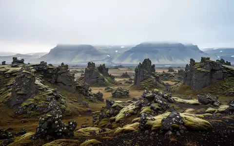 Eine weitläufige, moosbewachsene isländische Vulkanlandschaft mit nebligen Bergen im Hintergrund bei sanftem Tageslicht. - Foto: über boerse-global.de