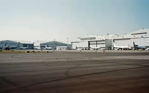 Weitläufiges Rollfeld vor einer Reihe von Flugzeughangars an einem Flughafen bei Tageslicht. - Foto: über boerse-global.de
