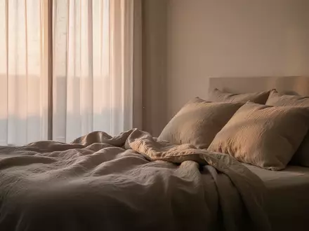 Ein ruhiges, minimalistisches Schlafzimmer bei Tagesanbruch mit weichem, natürlichem Licht, das auf ein ungemachtes Bett mit Leinenbettwäsche fällt. - Foto: über boerse-global.de
