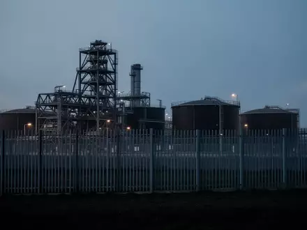 Eine weitläufige Industrieanlage in der Dämmerung, umzäunt von einem hohen Metallzaun, als Symbol für erhöhte Sicherheitsvorkehrungen. - Foto: über boerse-global.de