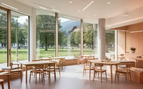 Ein heller, moderner Gemeinschaftsraum mit Holzmöbeln und Blick ins Grüne in einem österreichischen Gemeindezentrum. - Foto: über boerse-global.de