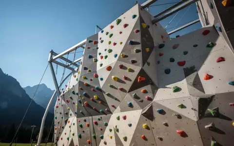 Moderne Außenkletterwand mit bunten Klettergriffen vor einem klaren Himmel in Oberbayern. - Foto: über boerse-global.de