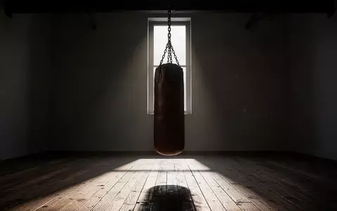 Ein leerer, schattiger Boxraum mit einem einzelnen Boxsack in einem minimalistischen, kargen Trainingsumfeld. - Foto: über boerse-global.de