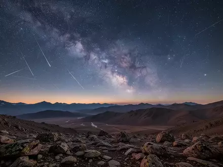 Eine weite, nächtliche Berglandschaft unter einem klaren Sternenhimmel mit sichtbaren Satellitenspuren am Horizont. - Foto: über boerse-global.de