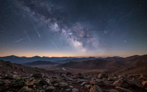 Eine weite, nächtliche Berglandschaft unter einem klaren Sternenhimmel mit sichtbaren Satellitenspuren am Horizont. - Foto: über boerse-global.de