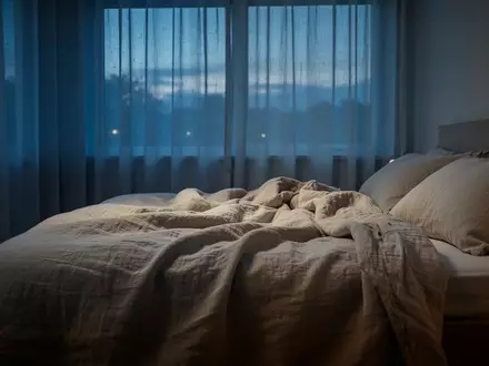 Ein minimalistisch eingerichtetes Schlafzimmer in der Abenddämmerung mit weichem Licht und gemütlichem Bett. - Foto: über boerse-global.de