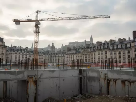 Eine Baustelle in der Kölner Innenstadt mit einem Baukran vor einem bewölkten Himmel und freigelegten Fundamenten. - Foto: über boerse-global.de