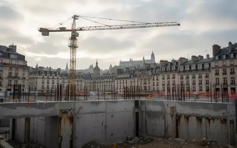 Eine Baustelle in der Kölner Innenstadt mit einem Baukran vor einem bewölkten Himmel und freigelegten Fundamenten. - Foto: über boerse-global.de