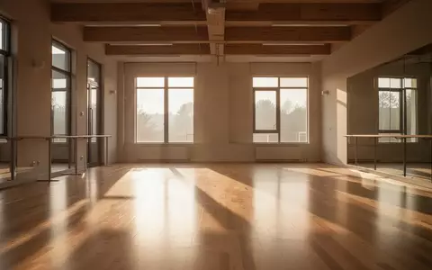 Ein lichtdurchfluteter, leerer Übungsraum mit Holzboden und großen Fenstern in einer minimalistischen Architektur. - Foto: über boerse-global.de
