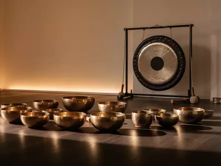 Ein minimalistischer Meditationsraum mit Klangschalen und einem Gong auf einem Holzboden in warmem Licht. - Foto: über boerse-global.de
