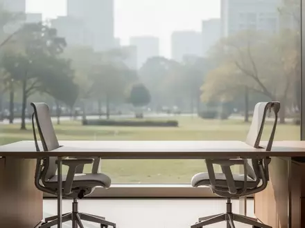 Ein leerer, sonnendurchfluteter Büroarbeitsplatz mit einem Schreibtisch vor einem Fenster, das auf einen ruhigen Park blickt. - Foto: über boerse-global.de