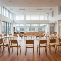 Ein heller, minimalistisch gestalteter Raum einer Bildungseinrichtung mit einem Stuhlkreis aus Holzstühlen und hellem Tageslicht. - Foto: über boerse-global.de