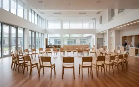 Ein heller, minimalistisch gestalteter Raum einer Bildungseinrichtung mit einem Stuhlkreis aus Holzstühlen und hellem Tageslicht. - Foto: über boerse-global.de