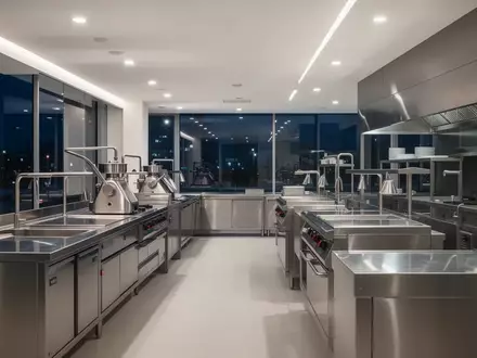 Moderne, minimalistische Edelstahl-Küchentechnik in einem hell erleuchteten Verkaufsraum bei Nacht. - Foto: über boerse-global.de