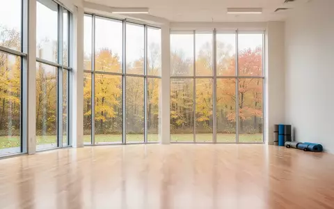 Ein heller, leerer Gymnastikraum mit Holzboden und Blick auf herbstliche Bäume durch große Fensterfronten. - Foto: über boerse-global.de