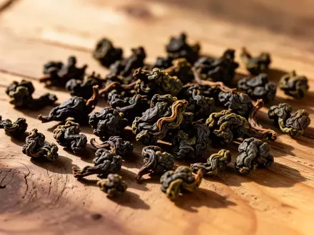 Getrocknete, dunkel geröstete Oolong-Teeblätter auf einer natürlichen Holzoberfläche bei warmem Licht. - Foto: über boerse-global.de