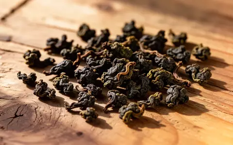 Getrocknete, dunkel geröstete Oolong-Teeblätter auf einer natürlichen Holzoberfläche bei warmem Licht. - Foto: über boerse-global.de