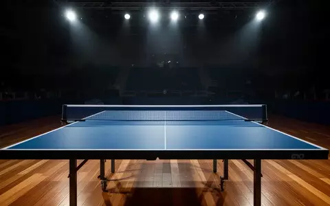 Ein leerer, professionell beleuchteter Tischtennistisch in einer großen, abgedunkelten Sporthalle. - Foto: über boerse-global.de