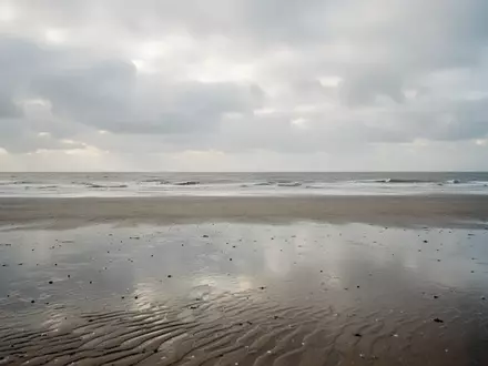 Ein weiter, leerer Sandstrand an der Nordsee unter einem bewölkten Herbsthimmel mit Blick auf das graue Meer. - Foto: über boerse-global.de