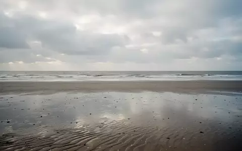 Ein weiter, leerer Sandstrand an der Nordsee unter einem bewölkten Herbsthimmel mit Blick auf das graue Meer. - Foto: über boerse-global.de