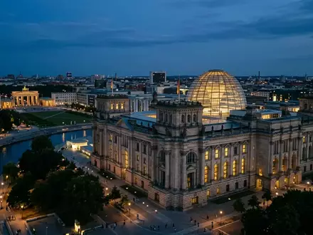 Das beleuchtete Reichstagsgebäude in Berlin bei Dämmerung unter einem klaren Abendhimmel. - Foto: über boerse-global.de