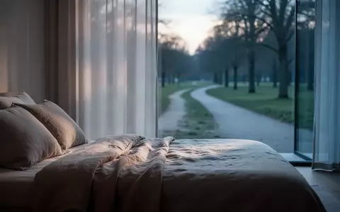 Ein minimalistisch eingerichtetes Schlafzimmer mit weichem Morgenlicht, das auf ein ordentlich gemachtes Bett fällt. - Foto: über boerse-global.de