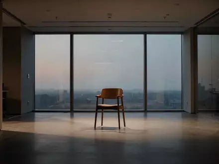 Ein leerer, minimalistischer Büroraum mit einem einzelnen Holzstuhl im Dämmerlicht, der eine ruhige und nachdenkliche Atmosphäre ausstrahlt. - Foto: über boerse-global.de