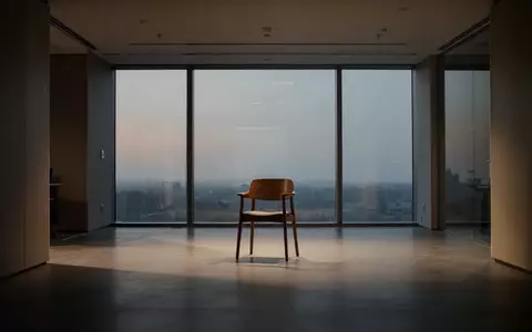 Ein leerer, minimalistischer Büroraum mit einem einzelnen Holzstuhl im Dämmerlicht, der eine ruhige und nachdenkliche Atmosphäre ausstrahlt. - Foto: über boerse-global.de