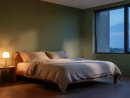 Ein minimalistisch eingerichtetes Schlafzimmer in gedeckten Farben mit weicher Bettwäsche und warmem Licht bei Dämmerung. - Foto: über boerse-global.de