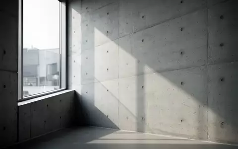 Ein minimalistischer Innenraum mit klaren architektonischen Linien und weichem Tageslicht, das geometrische Schatten auf eine Betonwand wirft. - Foto: über boerse-global.de
