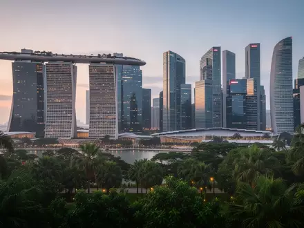 Die Skyline von Singapur bei Dämmerung mit moderner Architektur und üppiger Bepflanzung im Vordergrund. - Foto: über boerse-global.de