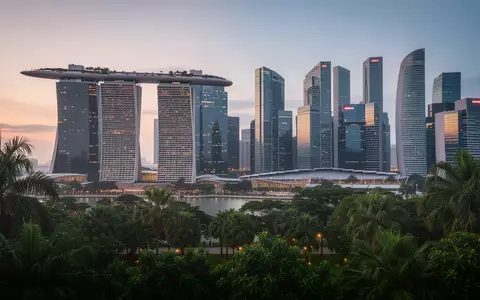 Die Skyline von Singapur bei Dämmerung mit moderner Architektur und üppiger Bepflanzung im Vordergrund. - Foto: über boerse-global.de