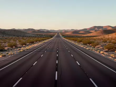 Eine leere, asphaltierte Fernstraße in einer weiten Wüstenlandschaft bei Sonnenuntergang. - Foto: über boerse-global.de