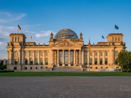 Das Berliner Reichstagsgebäude bei goldenem Sonnenlicht vor einem klaren Himmel. - Foto: über boerse-global.de