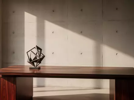 Ein minimalistischer Arbeitsplatz mit einem leeren Schreibtisch aus Mahagoniholz und einer abstrakten Skulptur. - Foto: über boerse-global.de