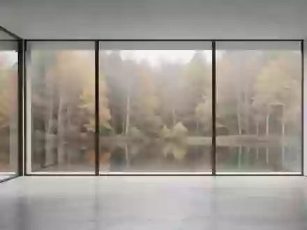 Ein minimalistischer, leerer Raum mit großen Fenstern und Blick auf einen herbstlichen Wald. - Foto: über boerse-global.de