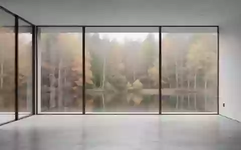 Ein minimalistischer, leerer Raum mit großen Fenstern und Blick auf einen herbstlichen Wald. - Foto: über boerse-global.de