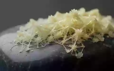 Nahaufnahme von kristallinen Schwefelstrukturen mit geometrischen Mustern auf einer dunklen Mineraloberfläche. - Foto: über boerse-global.de