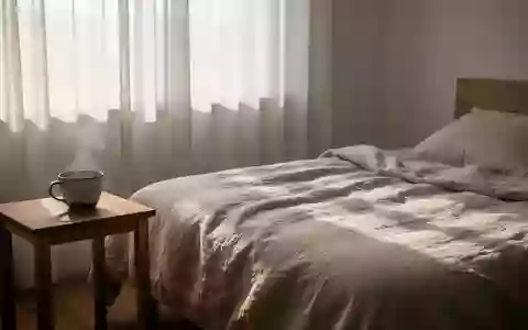 Ein minimalistisch eingerichtetes Schlafzimmer mit einer dampfenden Tasse Wasser auf einem Holztisch im sanften Morgenlicht. - Foto: über boerse-global.de