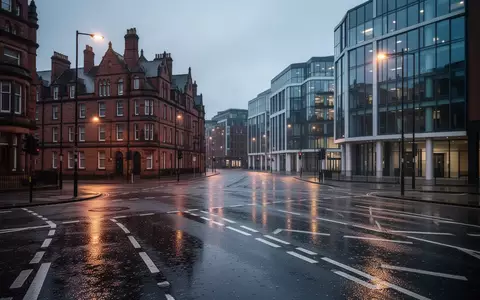 Eine regennasse Straßenkreuzung in Manchester bei Dämmerung mit einer Mischung aus historischer Ziegelarchitektur und moderner Glasfassade. - Foto: über boerse-global.de