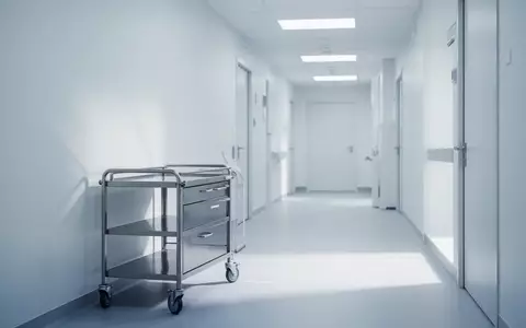 Ein minimalistisch eingerichteter, steriler medizinischer Untersuchungsraum mit sanftem Licht und einem leeren Metallwagen. - Foto: über boerse-global.de