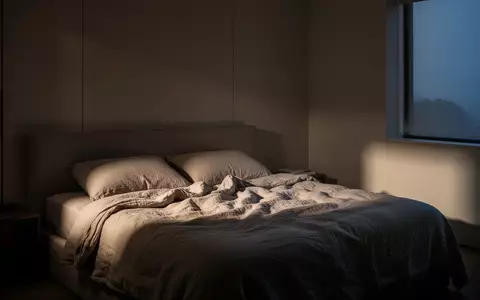 Ein minimalistisch eingerichtetes, ruhiges Schlafzimmer bei Dämmerlicht mit ungemachtem Bett und sanftem Lichteinfall. - Foto: über boerse-global.de