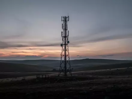 Ein einsamer Mobilfunkmast in einer hügeligen Landschaft bei Dämmerung. - Foto: über boerse-global.de