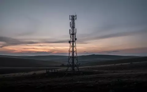 Ein einsamer Mobilfunkmast in einer hügeligen Landschaft bei Dämmerung. - Foto: über boerse-global.de