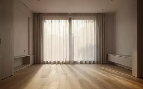 Ein minimalistisch eingerichtetes, leeres Wohnzimmer mit weichem Tageslicht, das durch Vorhänge auf den Holzboden fällt. - Foto: über boerse-global.de