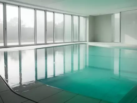 Ein leeres, helles Hallenbad mit ruhigem, blauem Wasser und natürlichem Lichteinfall. - Foto: über boerse-global.de