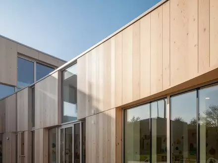 Helle, moderne Architektur einer Kindertagesstätte mit Holzfassade und großen Glasfronten bei natürlichem Tageslicht. - Foto: über boerse-global.de