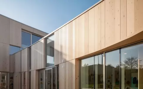 Helle, moderne Architektur einer Kindertagesstätte mit Holzfassade und großen Glasfronten bei natürlichem Tageslicht. - Foto: über boerse-global.de