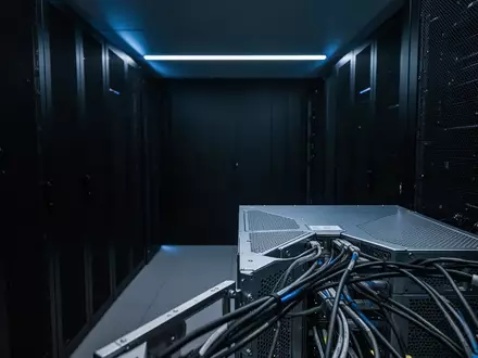 Ein minimalistischer, dunkel gehaltener Serverraum mit blauer Akzentbeleuchtung und Fokus auf die geometrischen Strukturen der Hardware. - Foto: über boerse-global.de